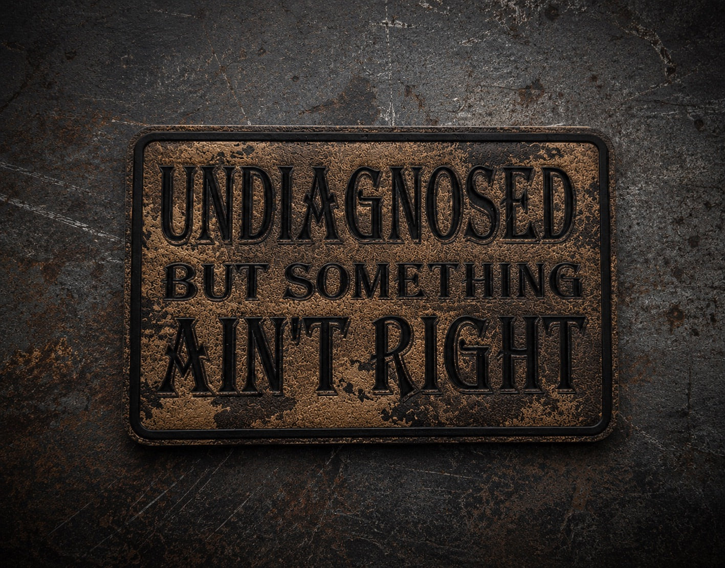 A rectangular vintage-style LEATHERETTE MORALE PATCH with distressed brown and black patina, featuring the text 'UNDIAGNOSED BUT SOMETHING AIN'T RIGHT' in black lettering, shown against a dark textured background.