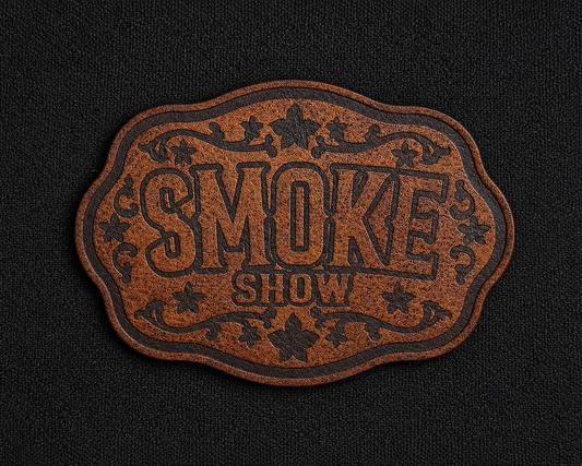 A brown textured leather morale patch with scalloped edges and the words 'SMOKE SHOW' in raised lettering, displayed on a black fabric background.