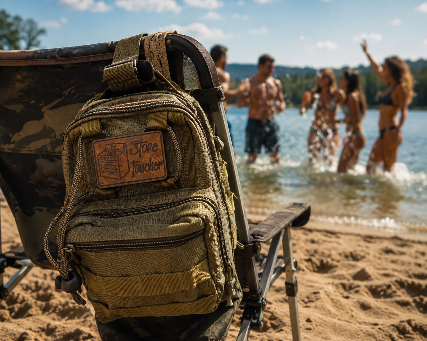 A tan and olive green tactical backpack with a 'Stove Toucher' patch is shown hanging from a camouflage folding chair on a sandy beach, with a blurred background of people swimming in a lake.